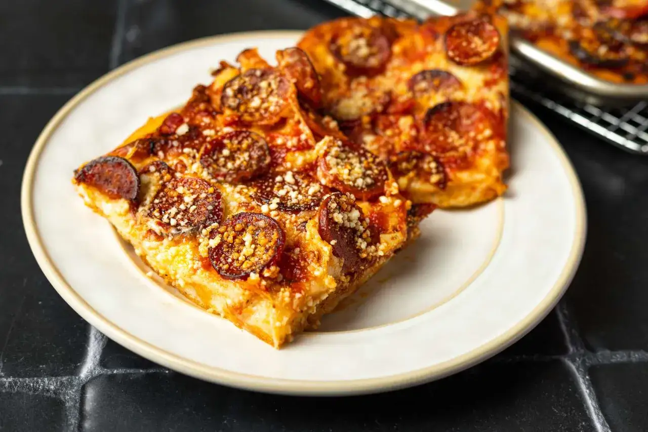 Zwei Stücke Pepperonipizza, frisch aus dem Ofen, auf einem Teller. Der Käse ist geschmolzen und die Wurst knusprig.