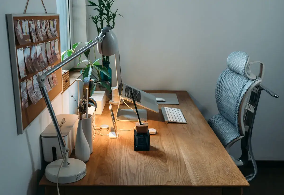 Ein gem&uuml;tliches Arbeitszimmer einrichten: Holztisch mit Laptop, Tastatur, Maus, Lampe, Pflanzen und einem bequemen B&uuml;rostuhl.