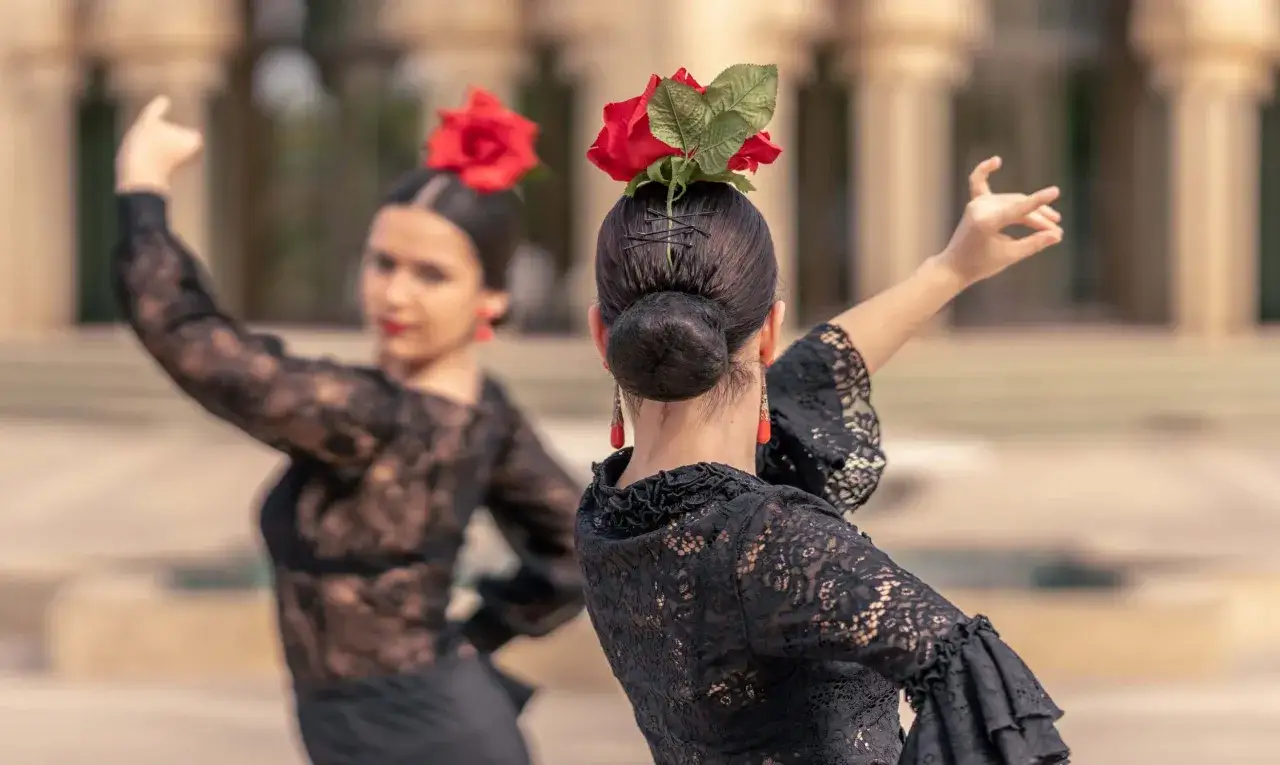 Dwie kobiety w czarnych, koronkowych strojach wykonują pełen pasji flamenco taniec, ozdobione czerwonymi różami we włosach.