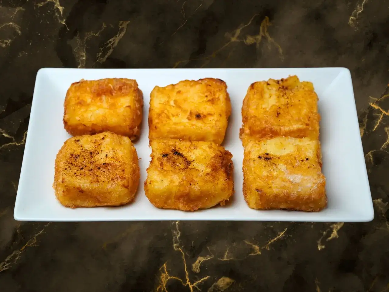 Seis porciones doradas de leche frita, con un toque de canela, listas para disfrutar.