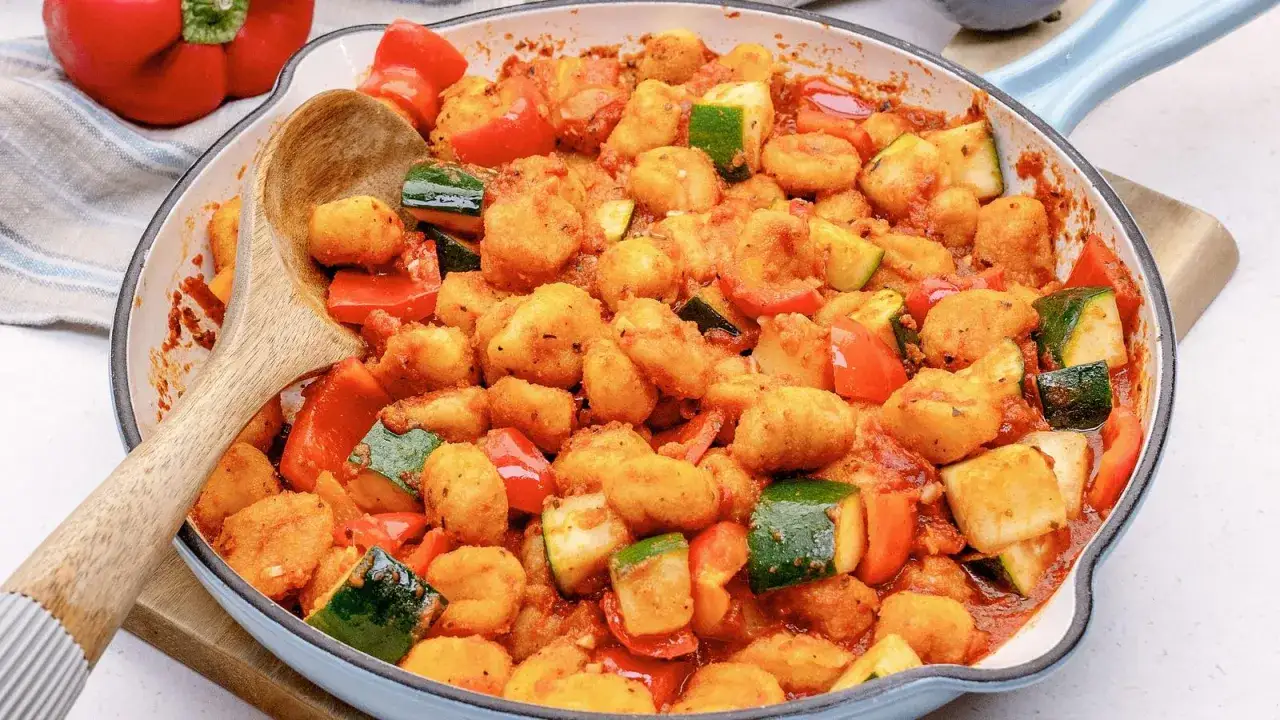 Herzhafte Gnocchi Pfanne mit Paprika und Zucchini in Tomatensauce, serviert mit einem Holzlöffel.