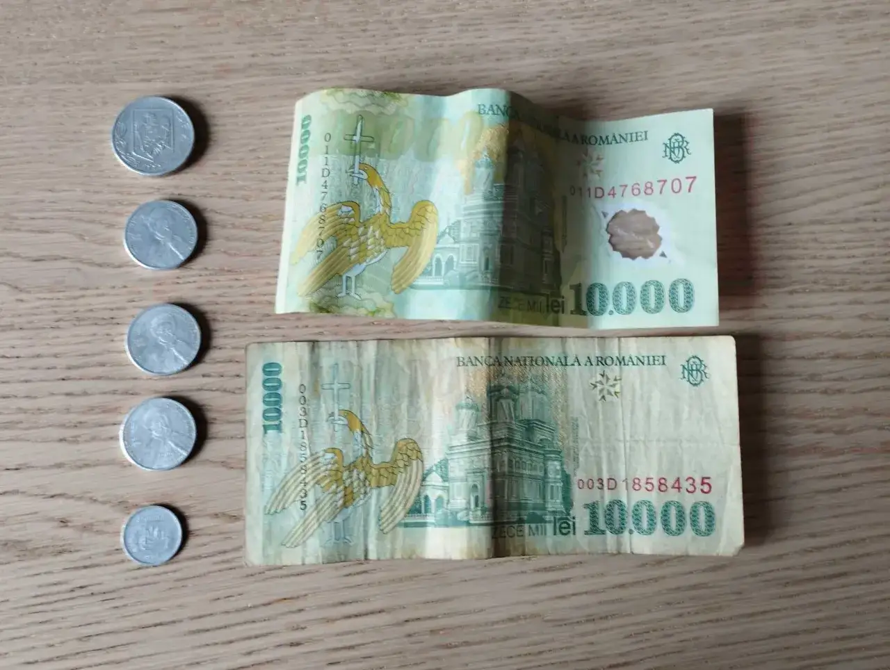 Dwie banknoty po 10 000 lejów, rumuńska waluta, leżą obok kilku monet.