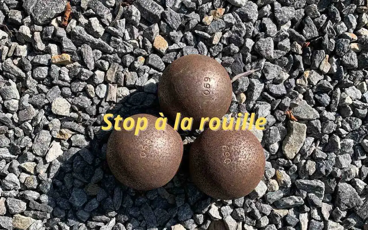 Trois boules de p&eacute;tanque rouill&eacute;es sur des graviers. Le texte 