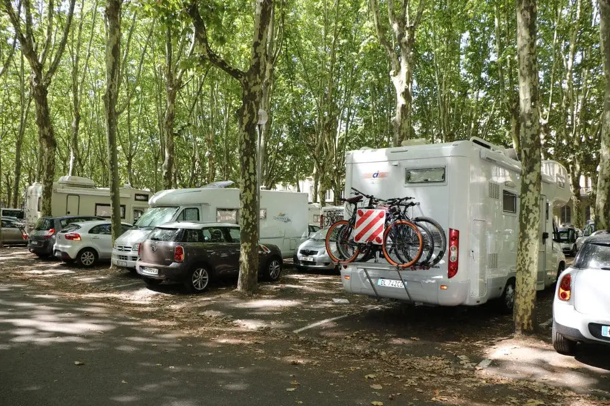 Stationnement de camping-cars sous les arbres, avec vélos à l'arrière d'un véhicule. Parking gratuit camping-car Bordeaux.