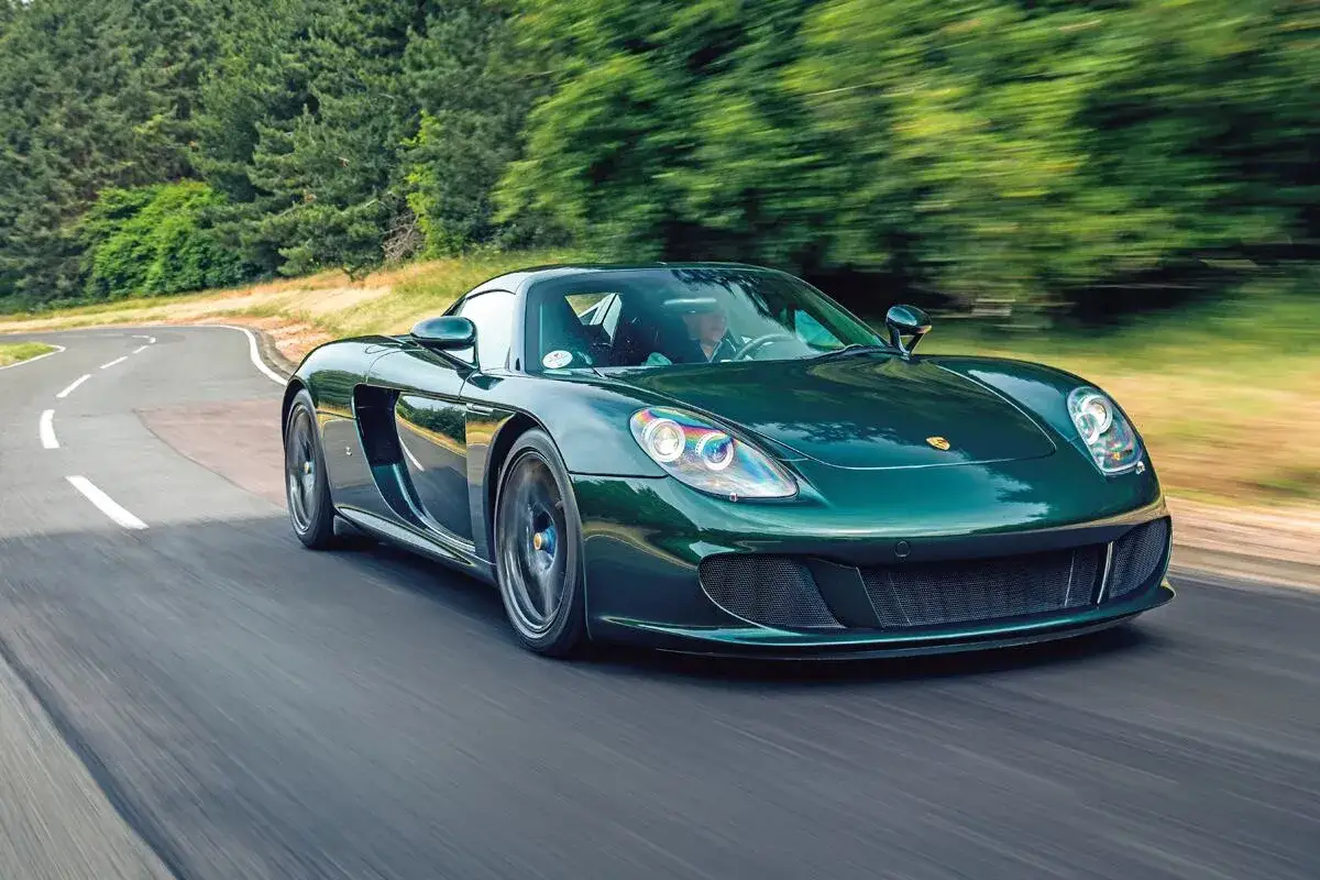 Zielony Porsche Carrera GT mknie po krętej drodze wśród drzew.