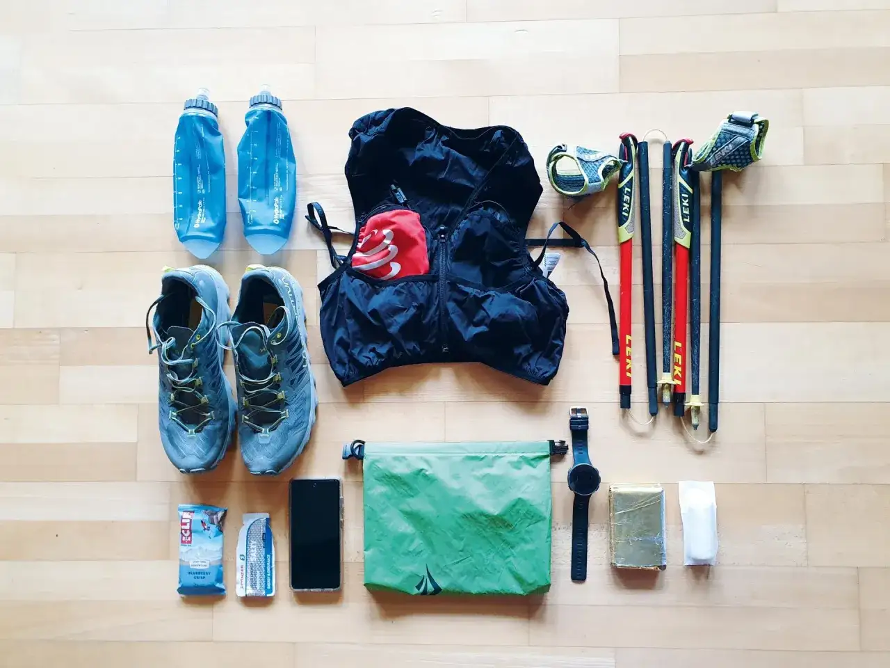 Équipement pour un ultra trailer : chaussures, gilets, bâtons Leki, bidons, téléphone, sac étanche, montre et barres énergétiques.