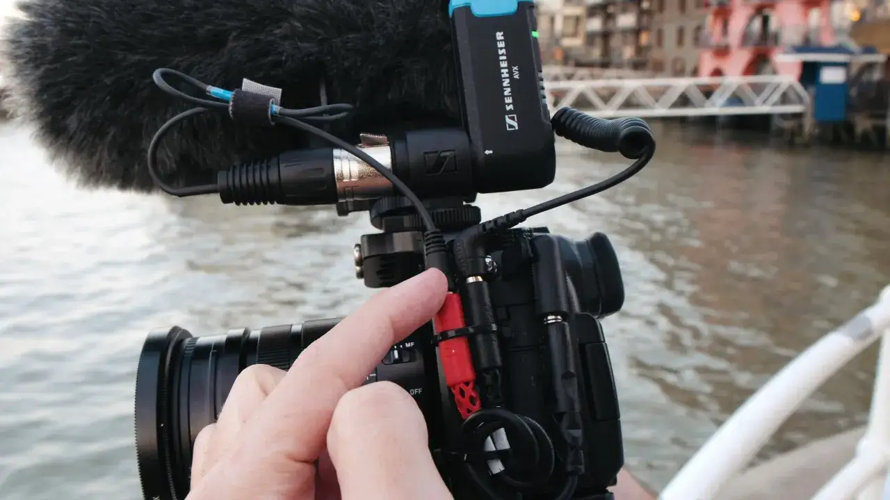 Mano che collega un cavo audio a una videocamera con microfono Sennheiser. L'attrezzatura è pronta per catturare suoni di alta qualità, forse per un documentario o un progetto gh5.