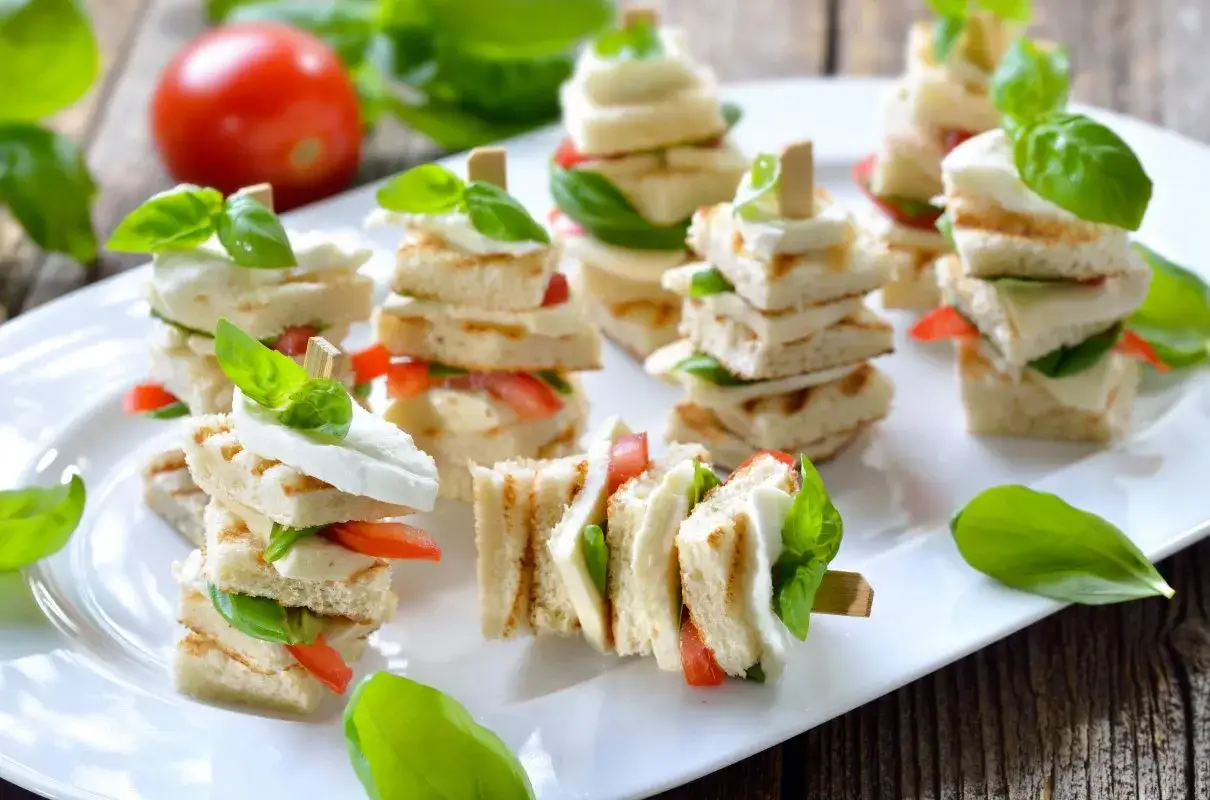 Mini kanapki z mozzarellą, pomidorem i bazylią na patyczkach – idealne przekąski na komunię.