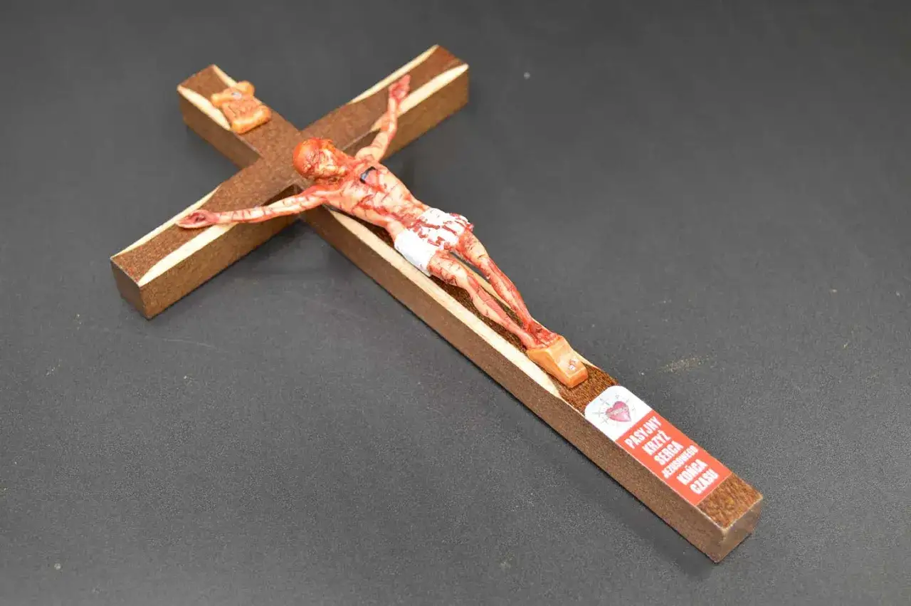 Drewniany krzyż z figurką Jezusa. Na belce krzyża wisi tekst: