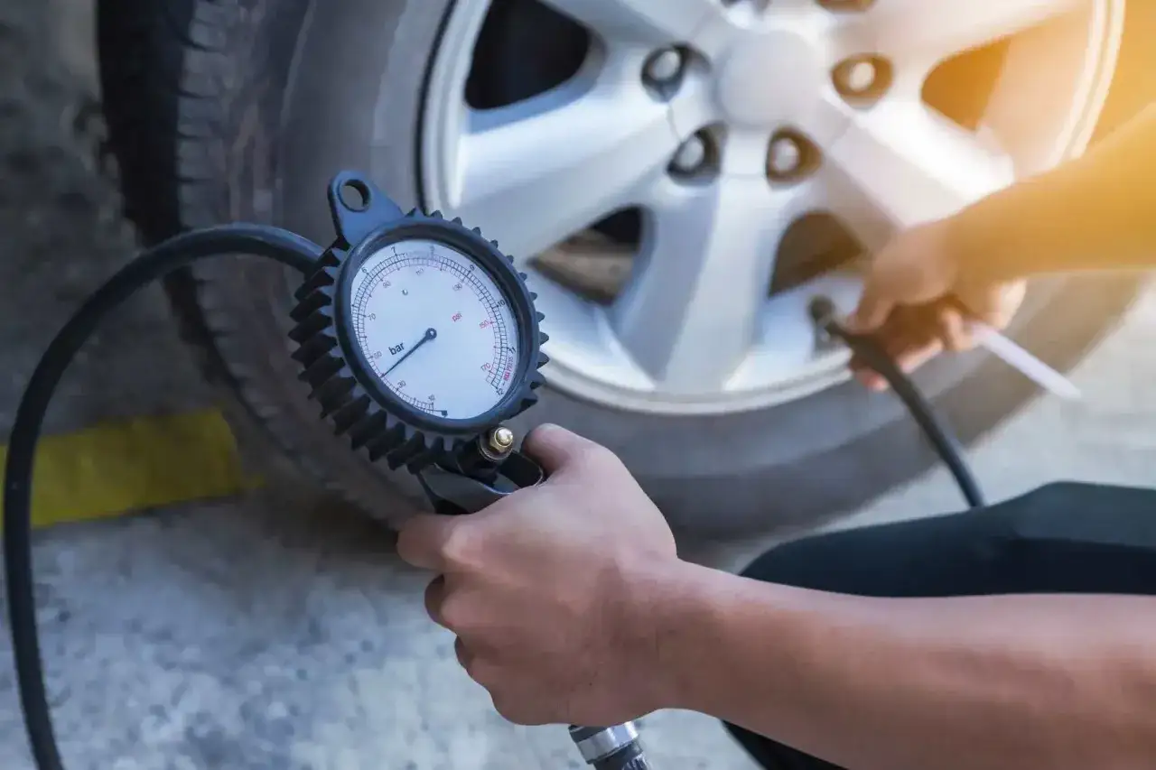 Contrôle de la pression pneu 225 45 r17 avec un manomètre. Un bras tient l'appareil près de la valve de la roue.