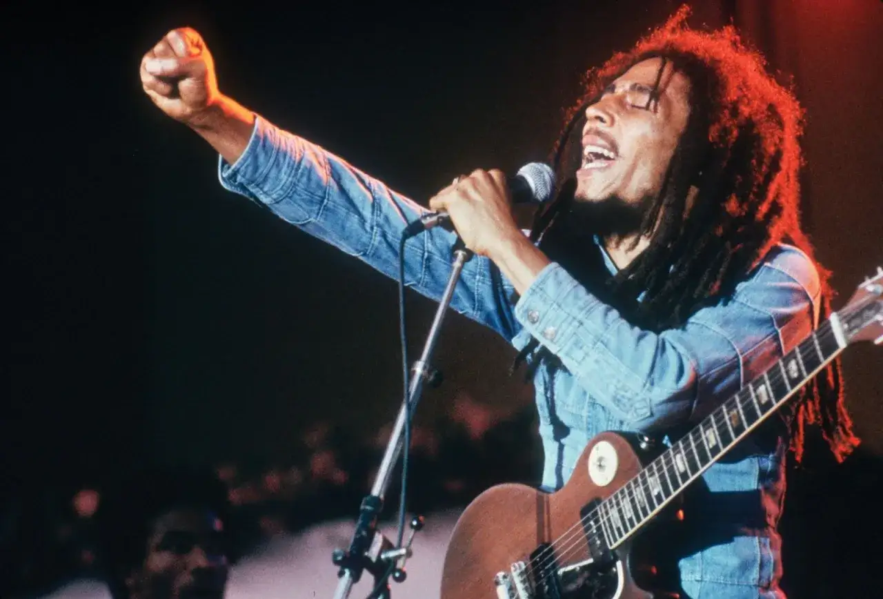 Bob Marley śpiewa z podniesioną pięścią, grając na gitarze. Jego styl i muzyka to kwintesencja rastafarianizmu, co to za ruch?