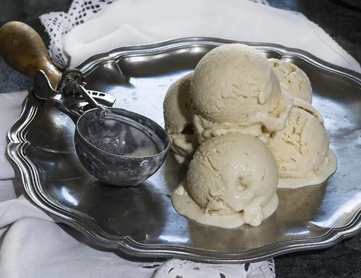 Bolas de helado de plátano derritiéndose en una bandeja de plata, junto a una cuchara para helado.