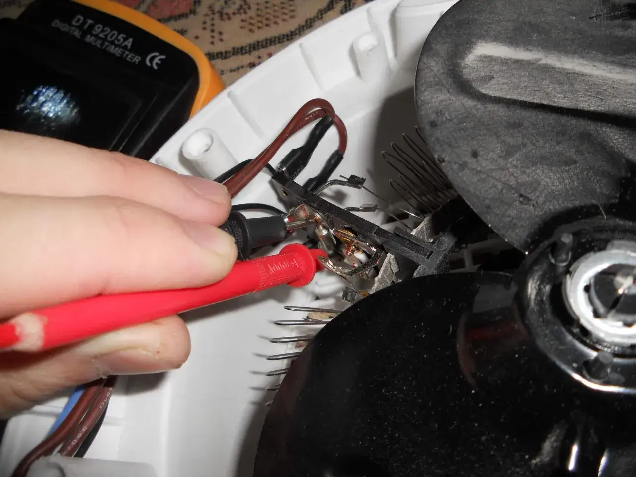 Ręka z sondami multimetru sprawdza połączenia elektryczne grzejnika. Pomocne przy próbie jak naprawić grzejnik elektryczny.