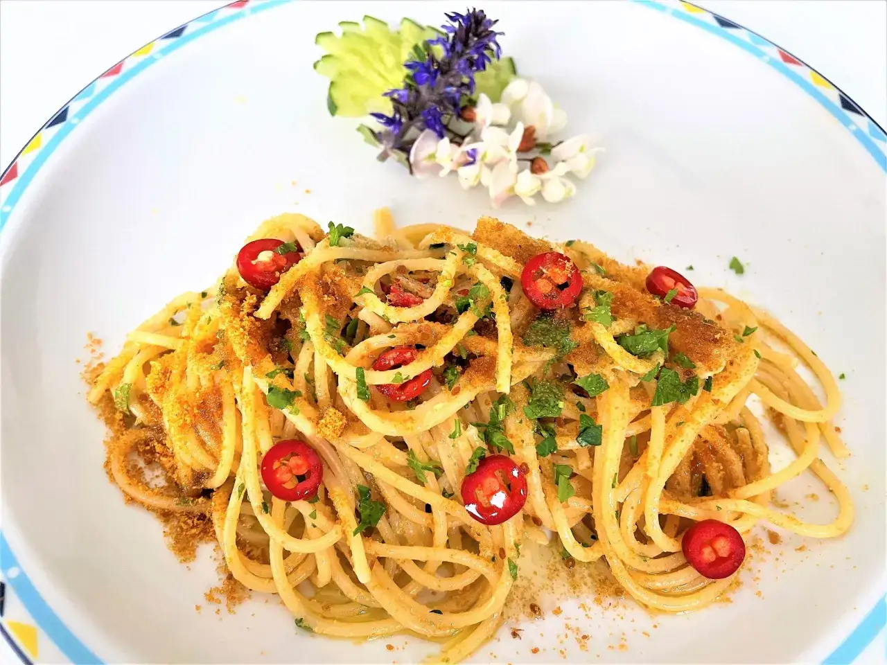 Spaghetti alla bottarga con peperoncino e prezzemolo, guarniti con fiori e cetriolo.