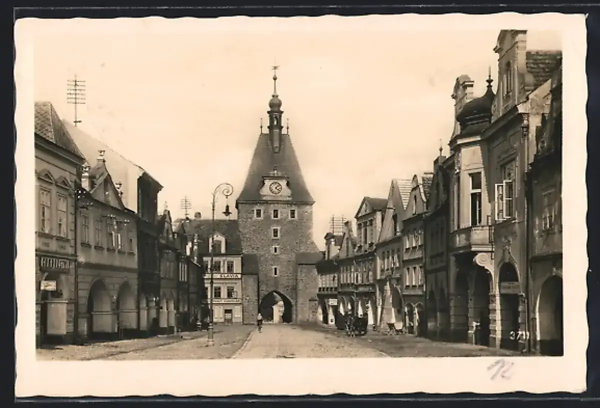 Historische Ansicht eines Marktplatzes mit einem Stadttor und Geb&auml;uden im **Tschechien**. Eine Kutsche und ein Radfahrer sind zu sehen.