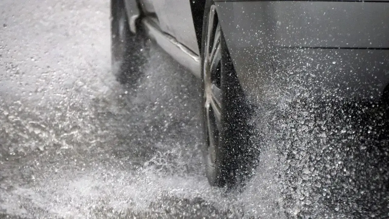 Koło samochodu wpada w kałużę, tworząc fontannę wody. To zjawisko to aquaplaning, czyli utrata przyczepności na mokrej nawierzchni.