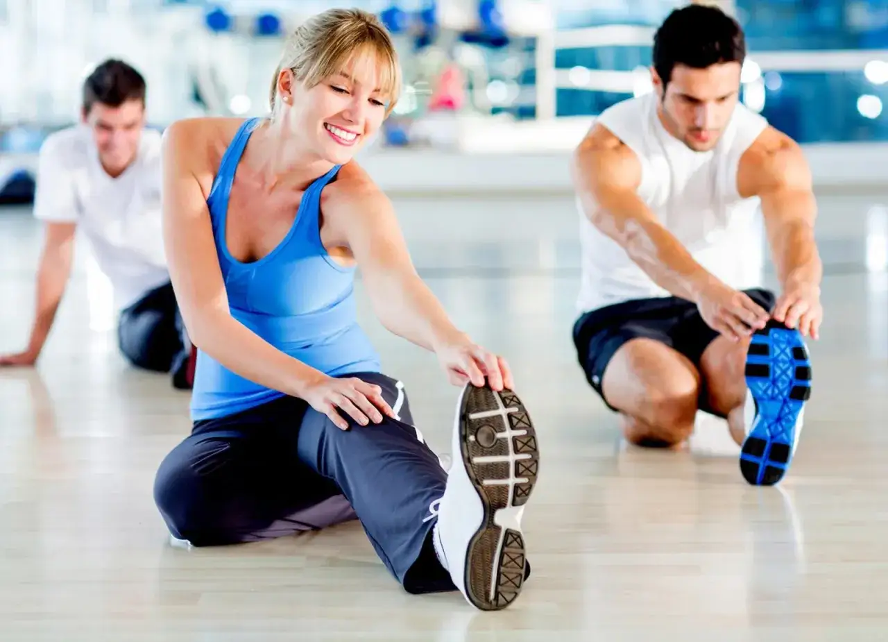 Uśmiechnięta kobieta i mężczyźni ćwiczą na siłowni. Zastanawiasz się, ile zarabia instruktor fitness?
