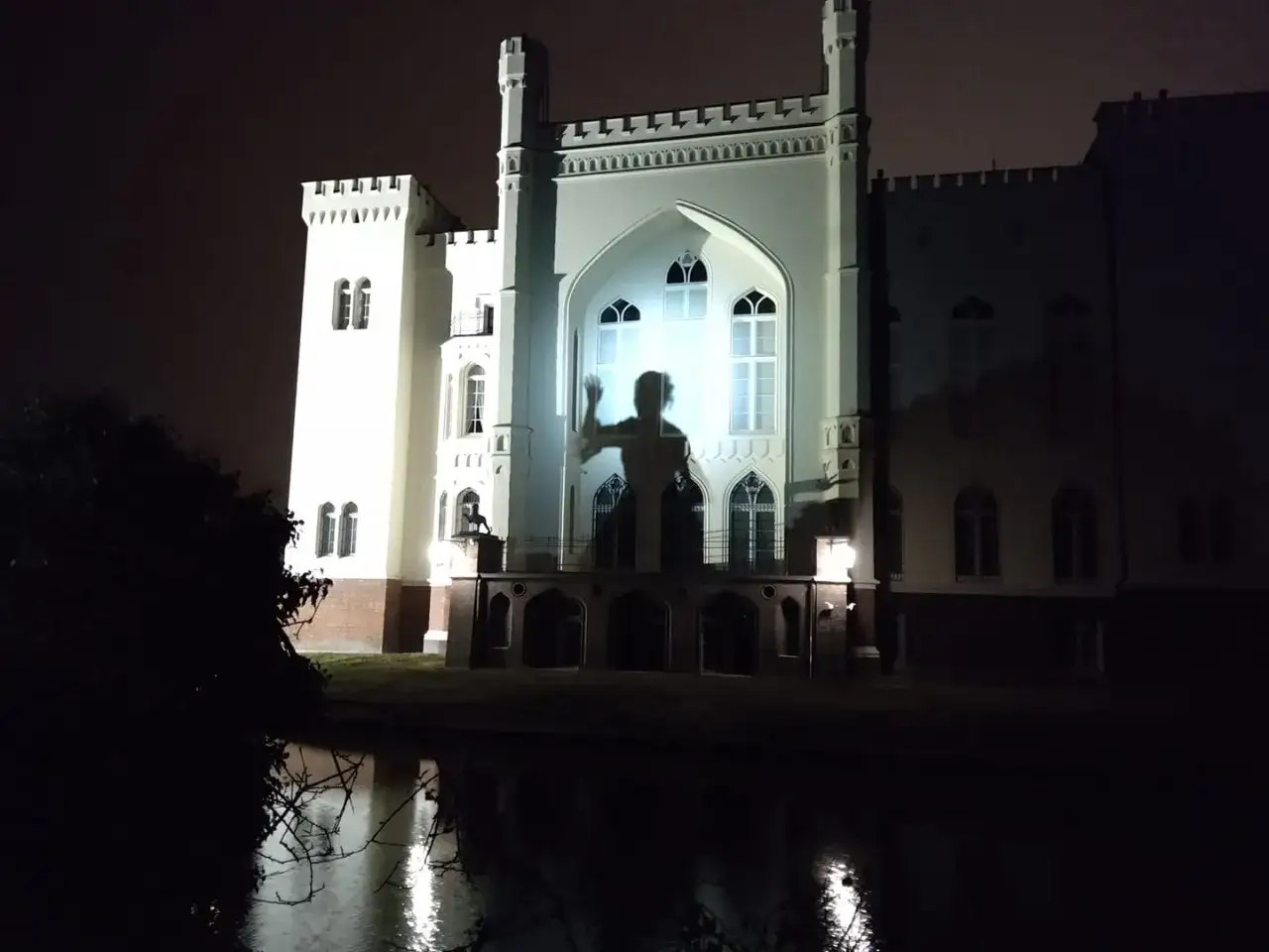 Widok zamku nocą, na fasadzie którego wyświetlono cień postaci, przypominający jak wygląda biała dama.