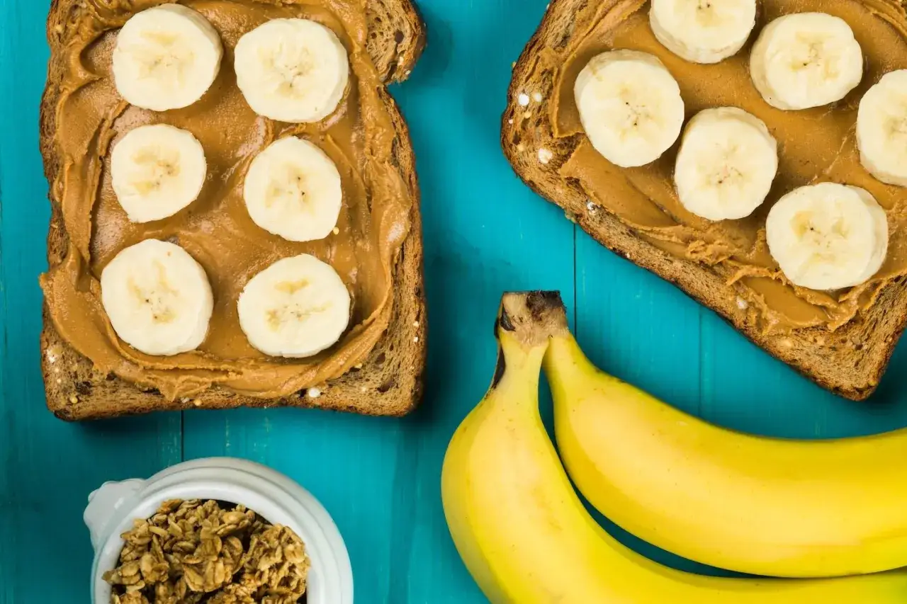Tartines de pain complet avec beurre de cacahu&egrave;te et rondelles de banane, id&eacute;ales pour savoir que manger avant une course. Bananes et granola &agrave; c&ocirc;t&eacute;.