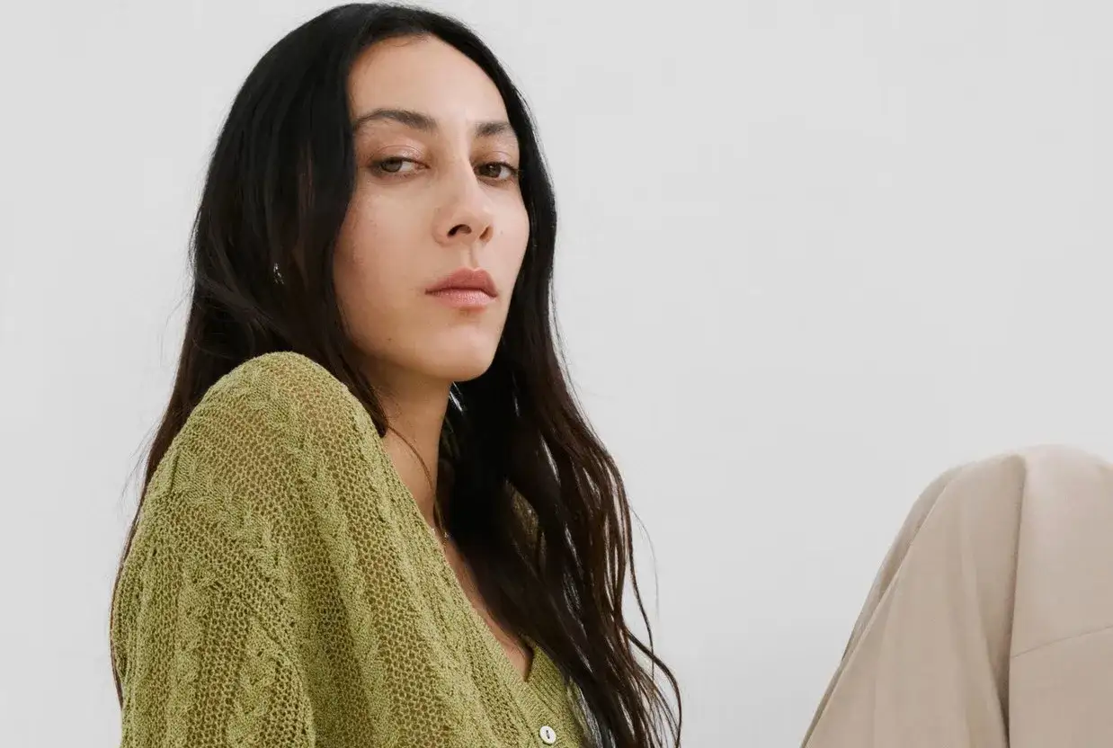Mujer con cabello oscuro y piel clara, viste un suéter tejido de un vibrante **el verde**.