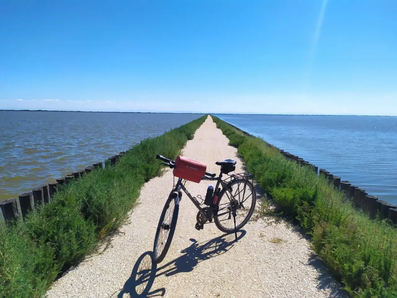 Bicicletta ferma su una **pista ciclabile** che si estende all'infinito tra acqua e cielo azzurro, un invito a esplorare il **Lido di Spina**.