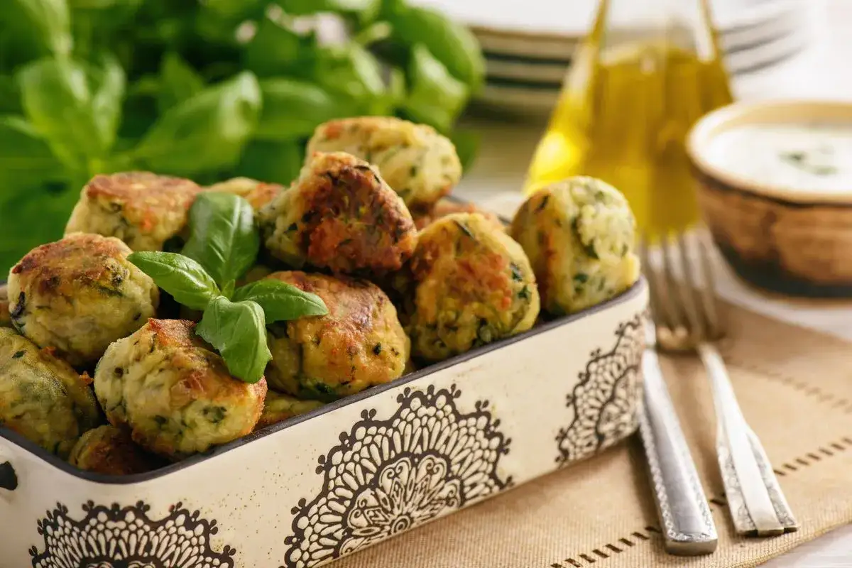 Crocchette di zucchine al forno dorate e profumate, guarnite con basilico fresco, servite in una ciotola decorata.