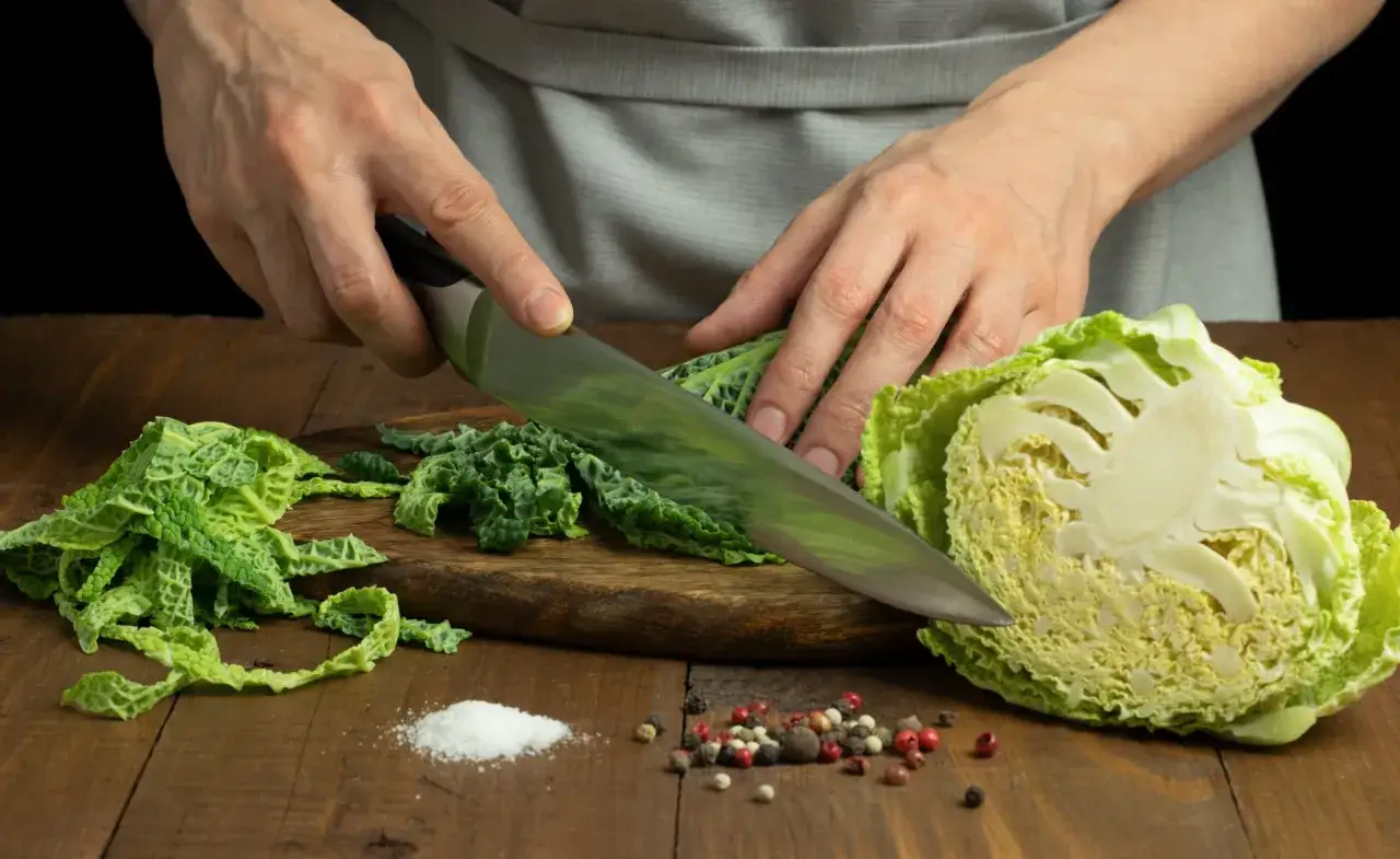 Hände schneiden Wirsing für ein leckeres wirsing rezept. Daneben liegen Salz und Pfefferkörner.