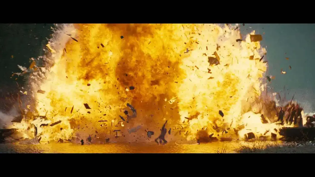 Potężna eksplozja w wodzie, jak w najlepszych **filmach akcji ostatnich lat**. Fragmenty latają w powietrzu, a w tle widać sylwetki ludzi.