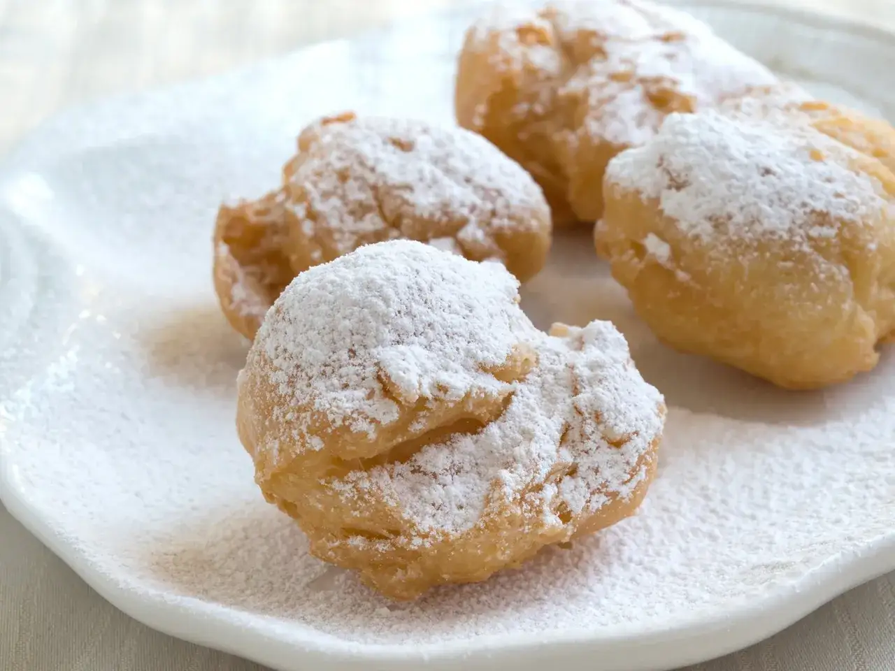 Vier goldbraune rheinische Krapfen, best&auml;ubt mit Puderzucker, liegen auf einem wei&szlig;en Teller.