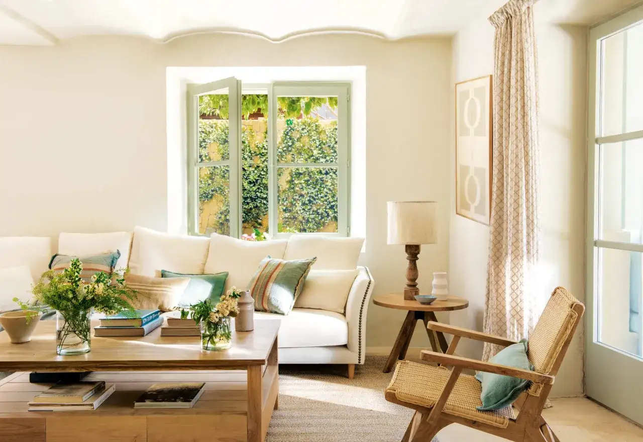 Sal&oacute;n luminoso con sof&aacute; blanco, mesa de centro de madera y **ventanas sin persianas soluciones** que dejan ver un jard&iacute;n exuberante.