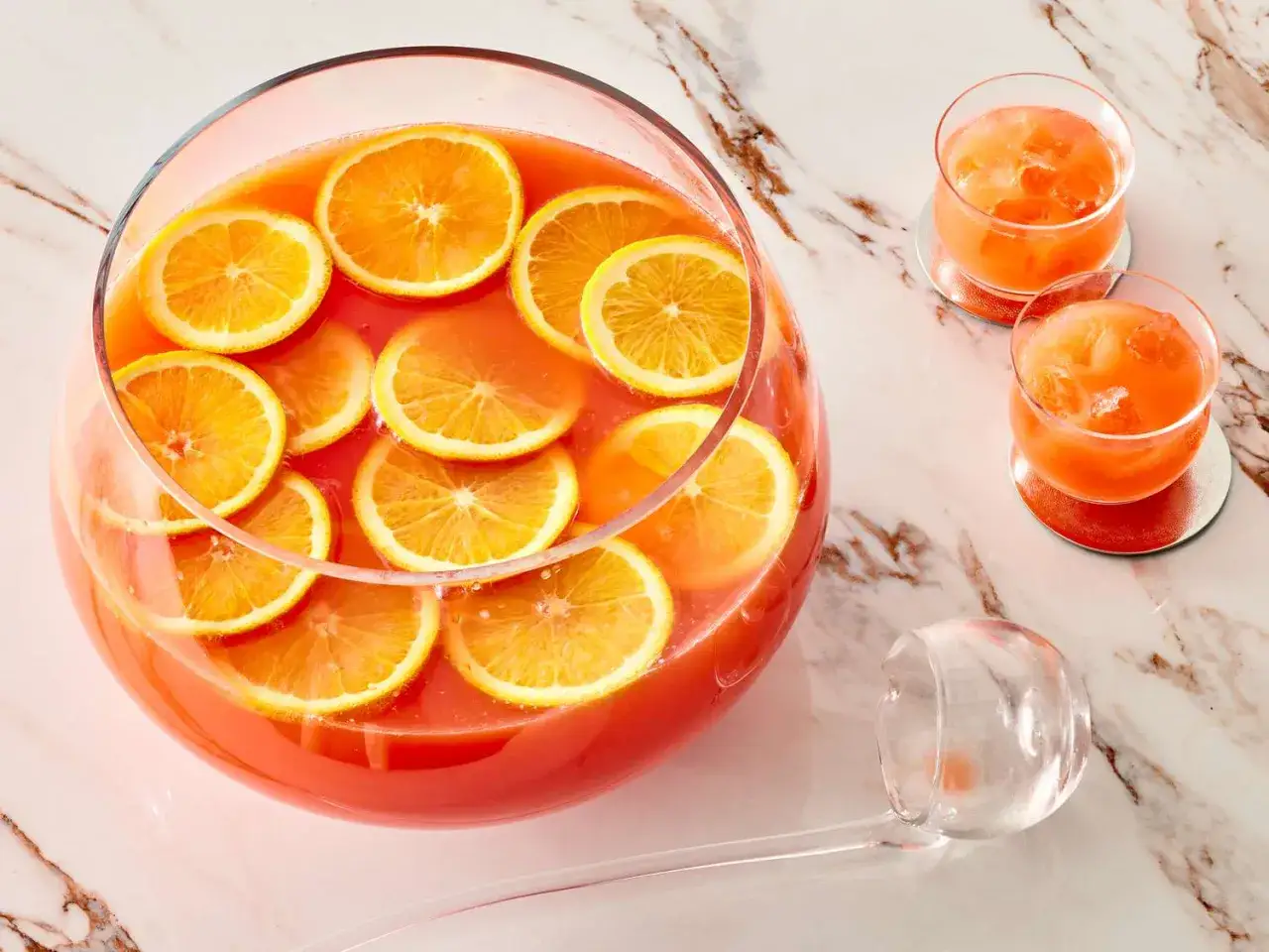 Orzeźwiający drink z fantą i plasterkami pomarańczy w dużej misie, obok dwa kieliszki z lodem. Idealny na letnie przyjęcie.