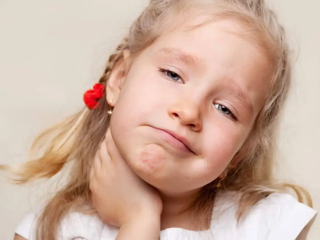 Bambina con espressione sofferente, si tocca la gola, possibili sintomi streptococco bambini.