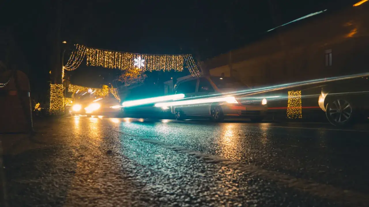 Voitures circulant la nuit sous des guirlandes lumineuses. Le feu de position seul des v&eacute;hicules cr&eacute;e des tra&icirc;n&eacute;es de lumi&egrave;re sur la chauss&eacute;e mouill&eacute;e.