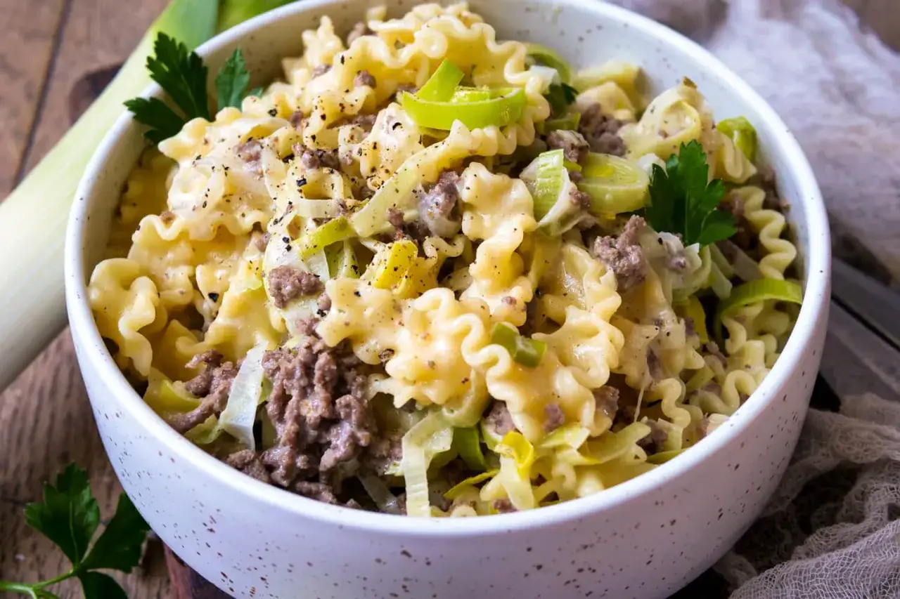 Herzhafte hackfleisch lauch pfanne mit cremiger Sauce und bunten Nudeln, garniert mit Petersilie.