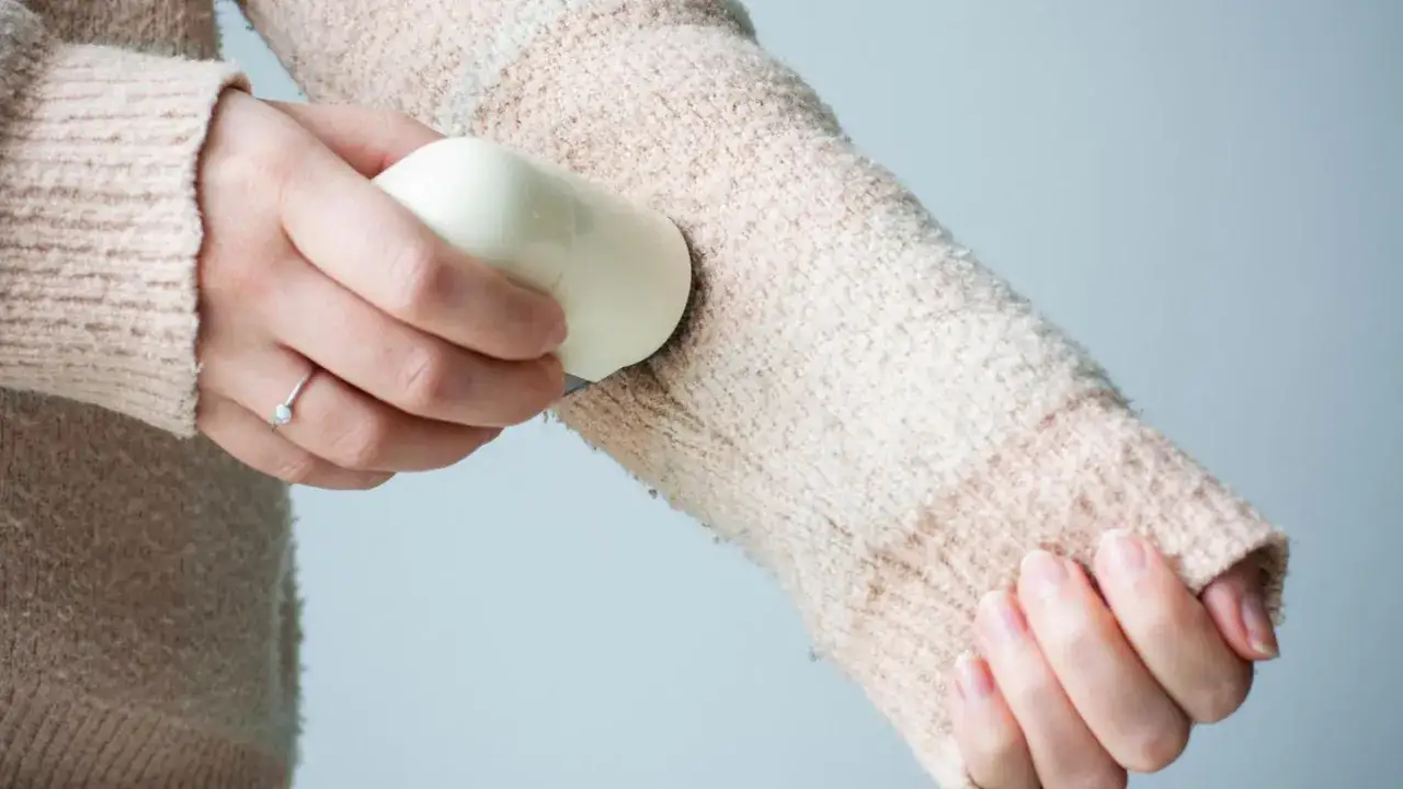 Eine Hand entfernt mit einem Fusselrasierer Fusseln von einem weichen Pullover. Der Mohair-Pullover fusselt und wird wieder glatt gemacht.