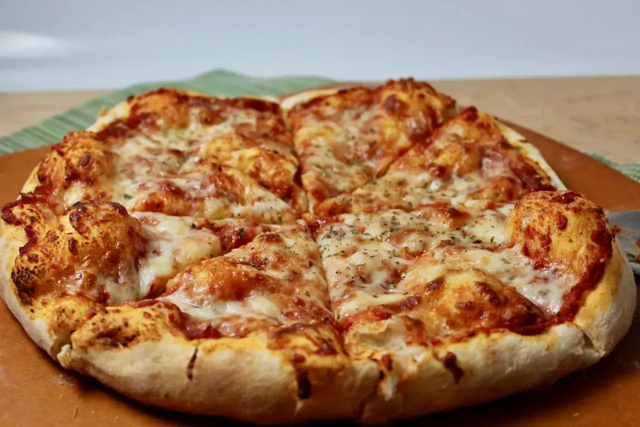 Pyszne, gorące pizza ciasto z ciągnącym się serem i aromatycznymi ziołami, pokrojone na kawałki.