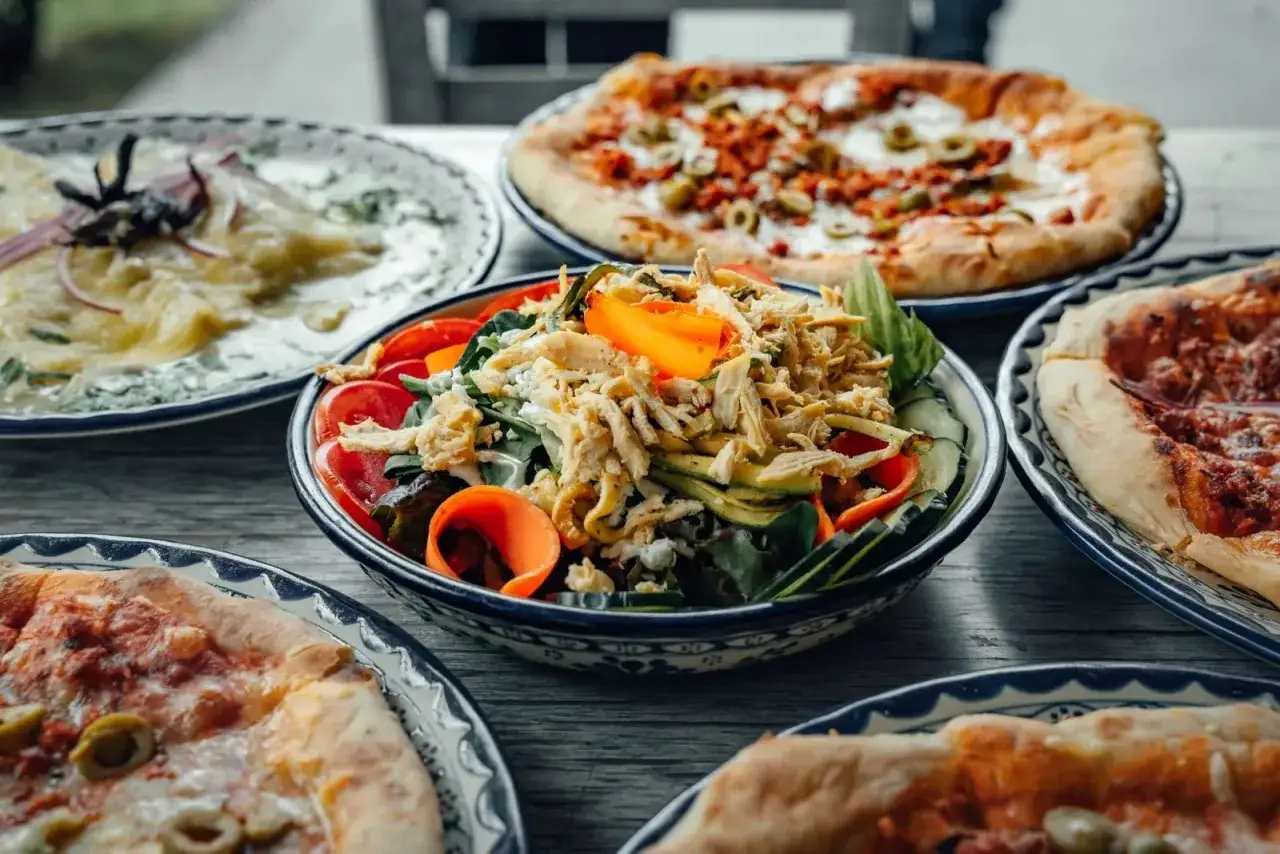Świeża sałatka z kurczakiem i warzywami to idealna propozycja, co podać do pizzy. Obok widać też inne pizze i danie z serem.