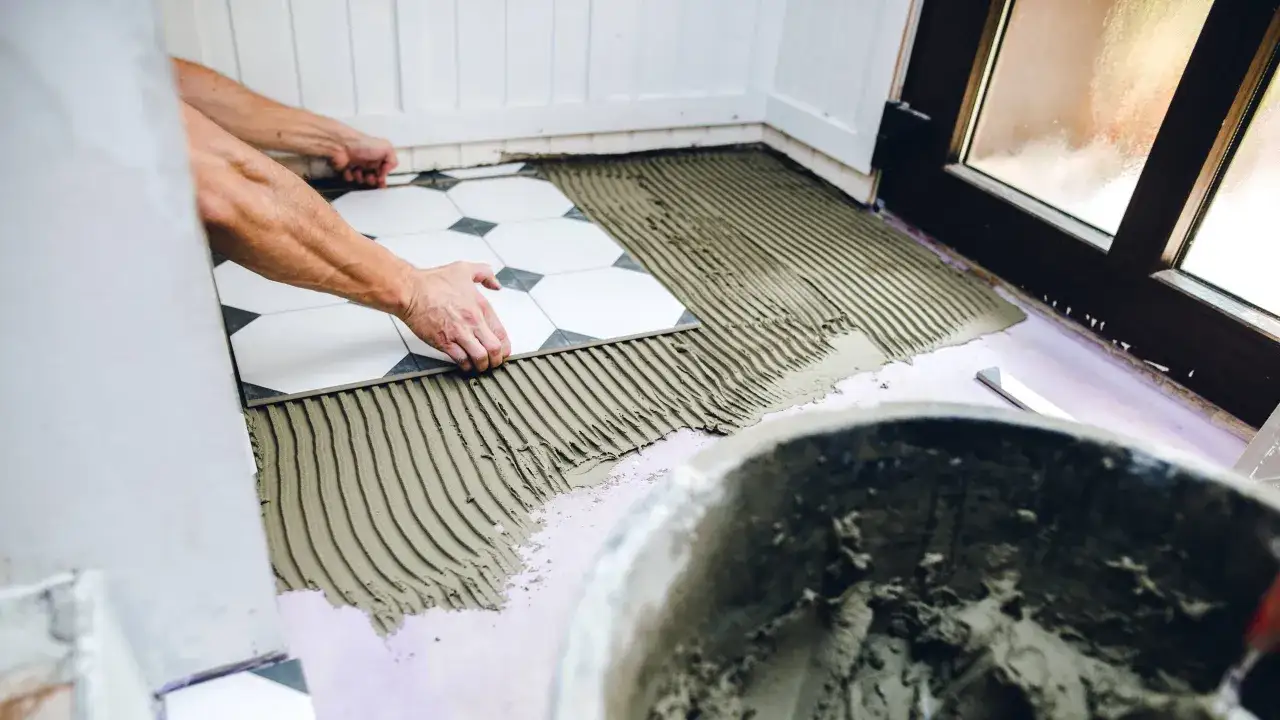 Manos colocando azulejos blancos y negros sobre cemento fresco.