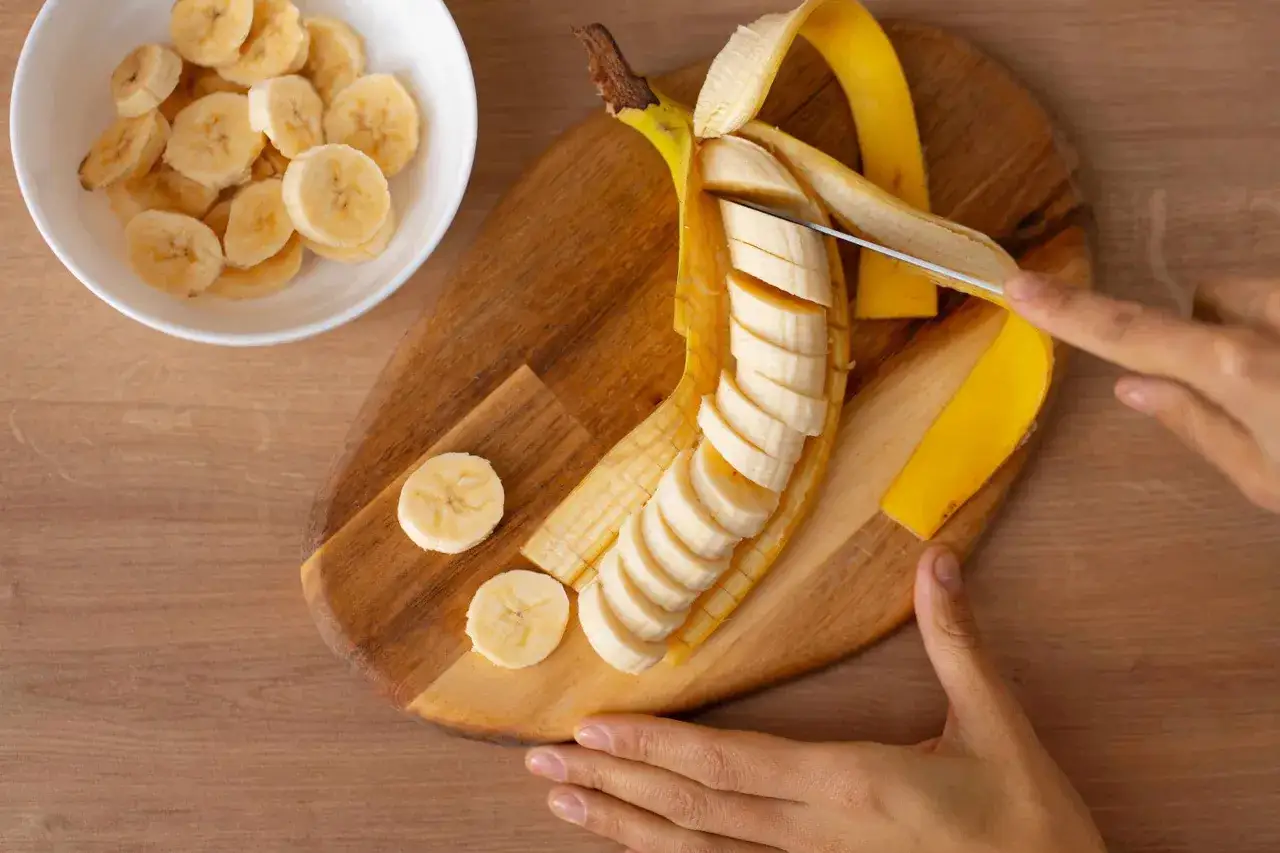 Bananenscheiben werden auf einem Holzbrett geschnitten. Eine Schüssel mit Scheiben steht daneben. Wie viel Kalium hat eine Banane?