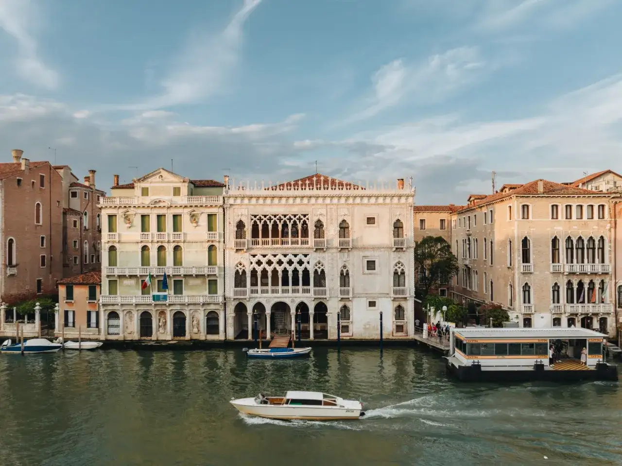 Palazzo Ca' d'Oro, un gioiello veneziano, si specchia nel Canal Grande. Barche scivolano sull'acqua, mentre il sole illumina la facciata dorata.