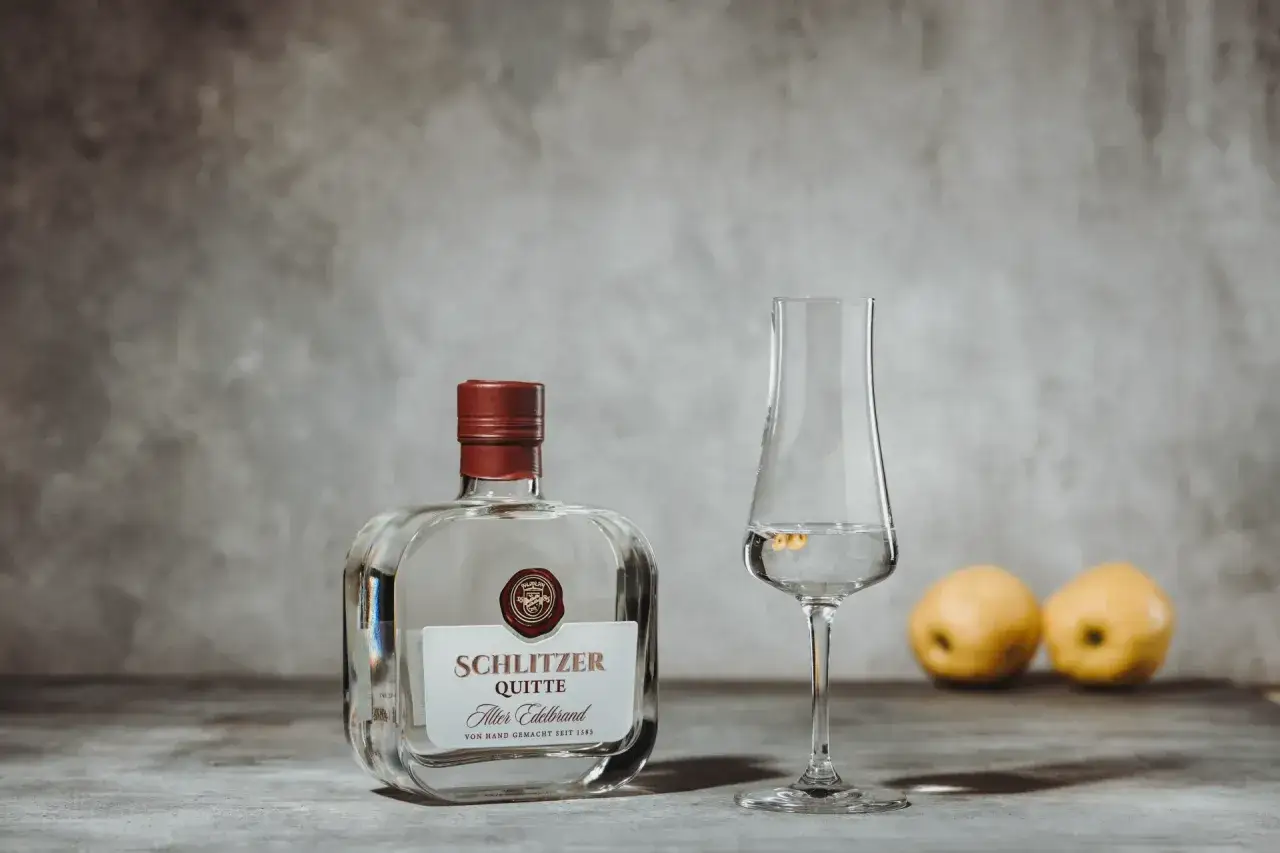 Flasche Schlitzer Quitte, ein Glas mit dem Edelbrand und zwei Quitten. Perfekt, um Quittenschnaps selber machen zu lernen.