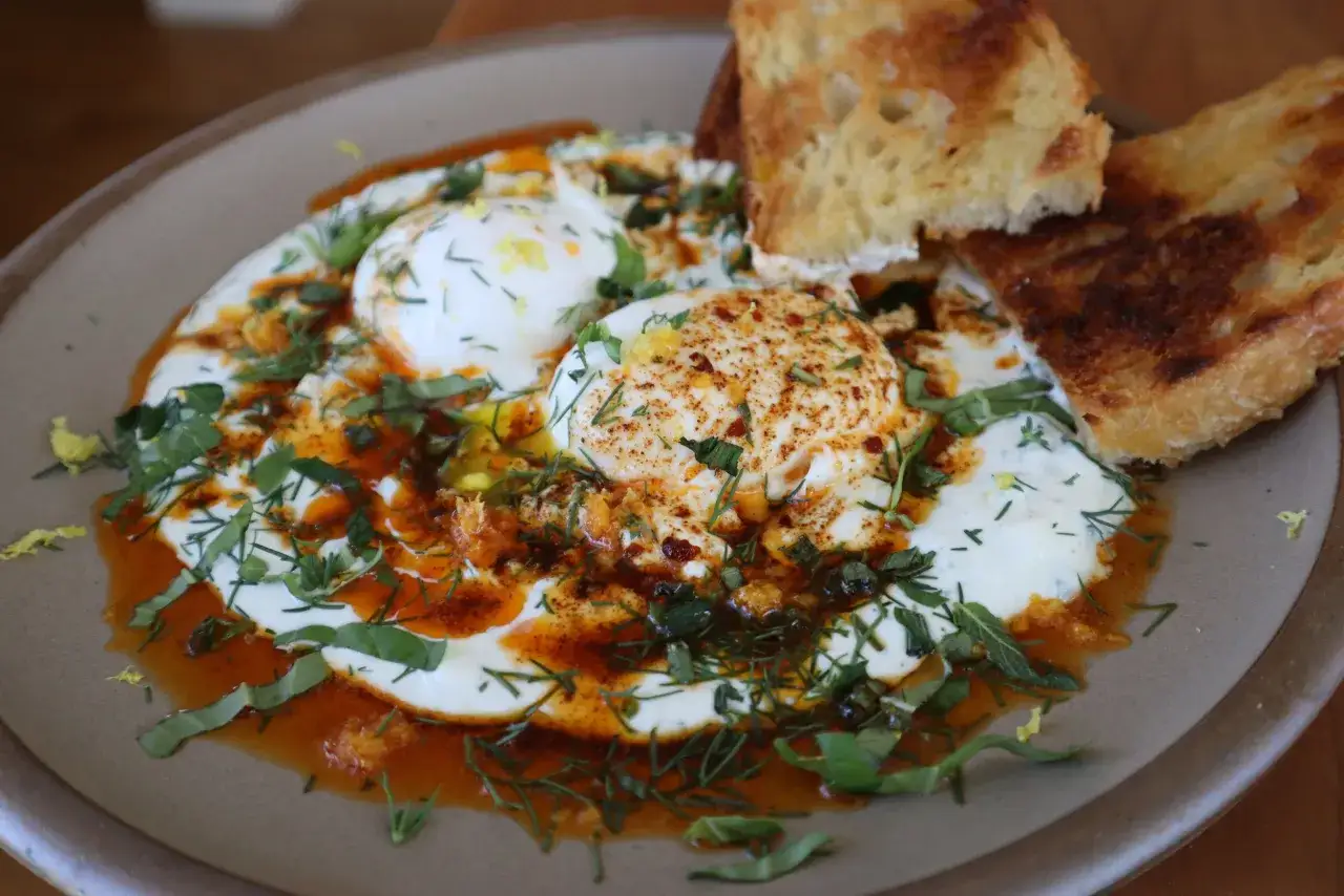 Œufs pochés sur un lit de yaourt, arrosés d'huile épicée et d'herbes fraîches. Une délicieuse recette de cilbir pour un brunch parfait.
