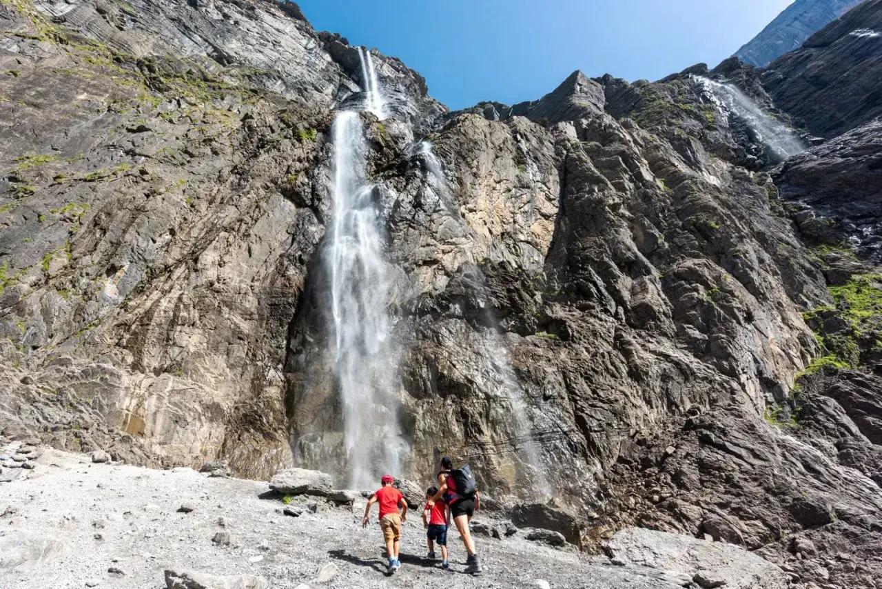 Famille en randonnée sur la ruta circo de Gavarnie, admirant la cascade spectaculaire tombant d'une falaise rocheuse.