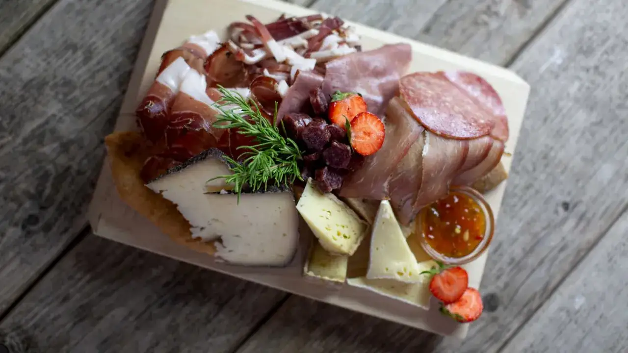 K&auml;seplatte mit italienischem Speck, Salami, Erdbeeren und Rosmarin auf Holzbrett.