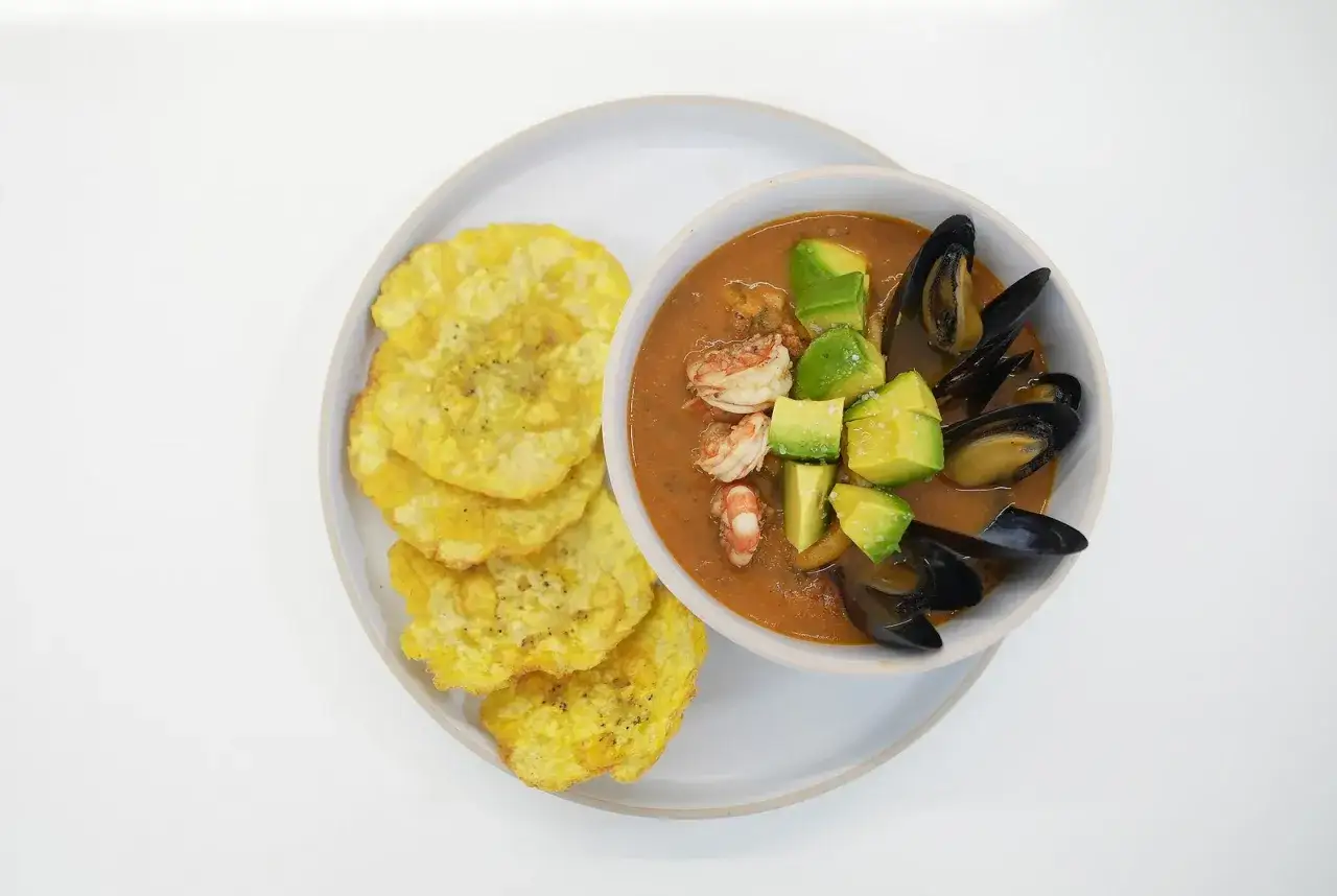 Delicioso plato de tostones crujientes junto a un taz&oacute;n de sopa marinera con camarones, mejillones y aguacate.