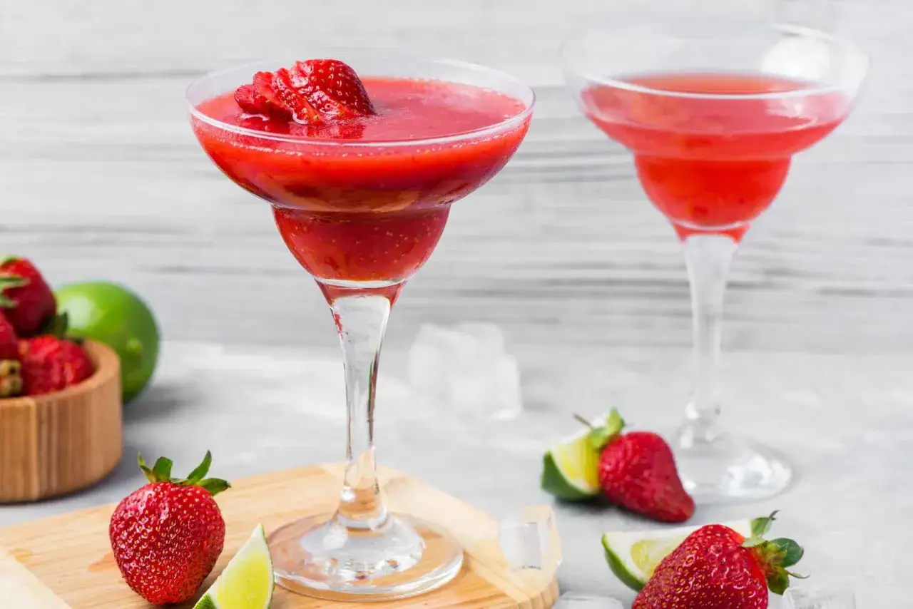 Två frostiga strawberry daiquiris, dekorerade med färska jordgubbar och lime, redo att avnjutas.