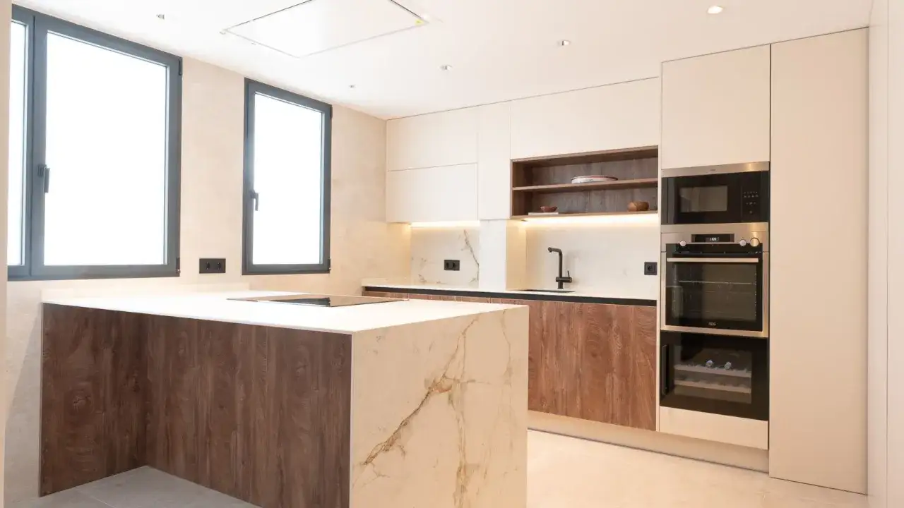 Elegantes cocinas modernas blancas con isla central de mármol y detalles en madera. Electrodomésticos integrados y luz ambiental.