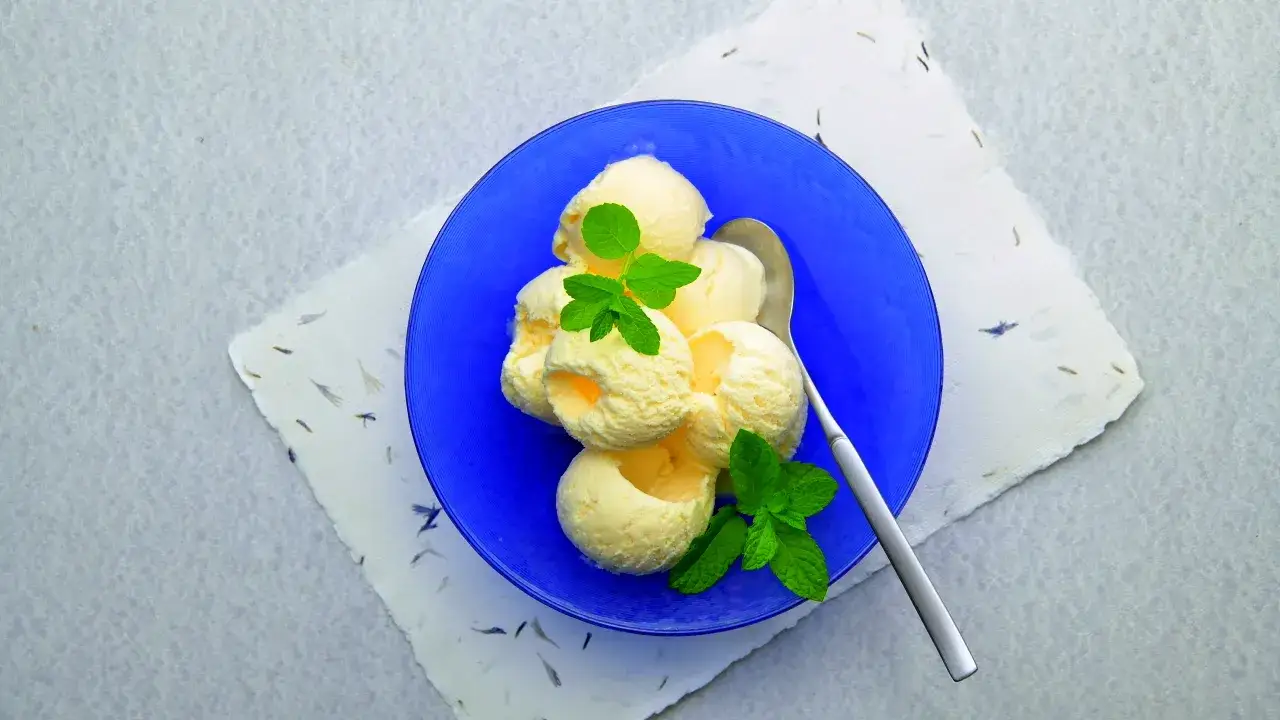 Kremowe lody po francusku, udekorowane listkami mięty, podane na niebieskim talerzyku.