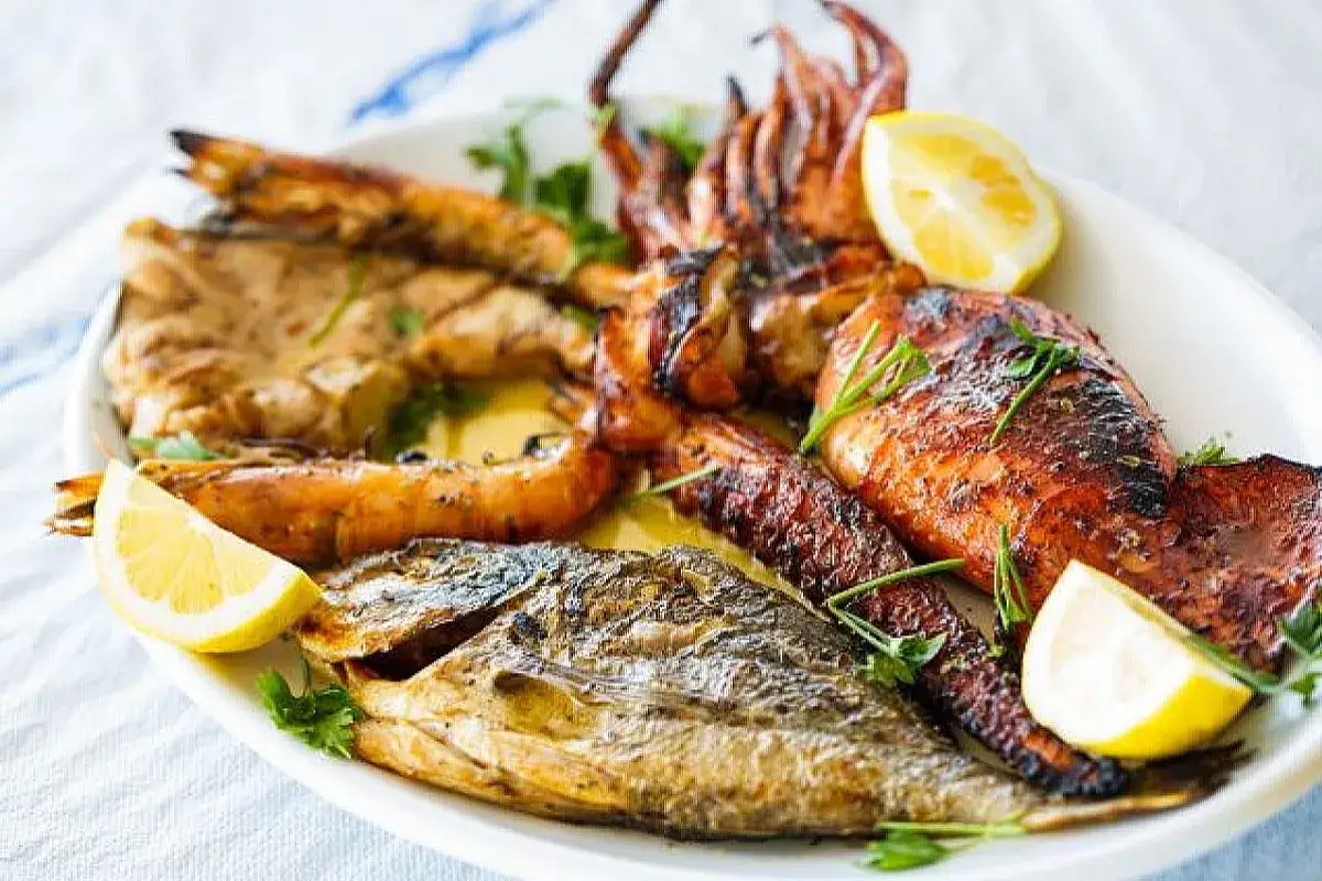 Un piatto invitante di grigliata di pesce: gamberi succulenti, calamari dorati e un pesce intero, guarniti con limone fresco e prezzemolo.