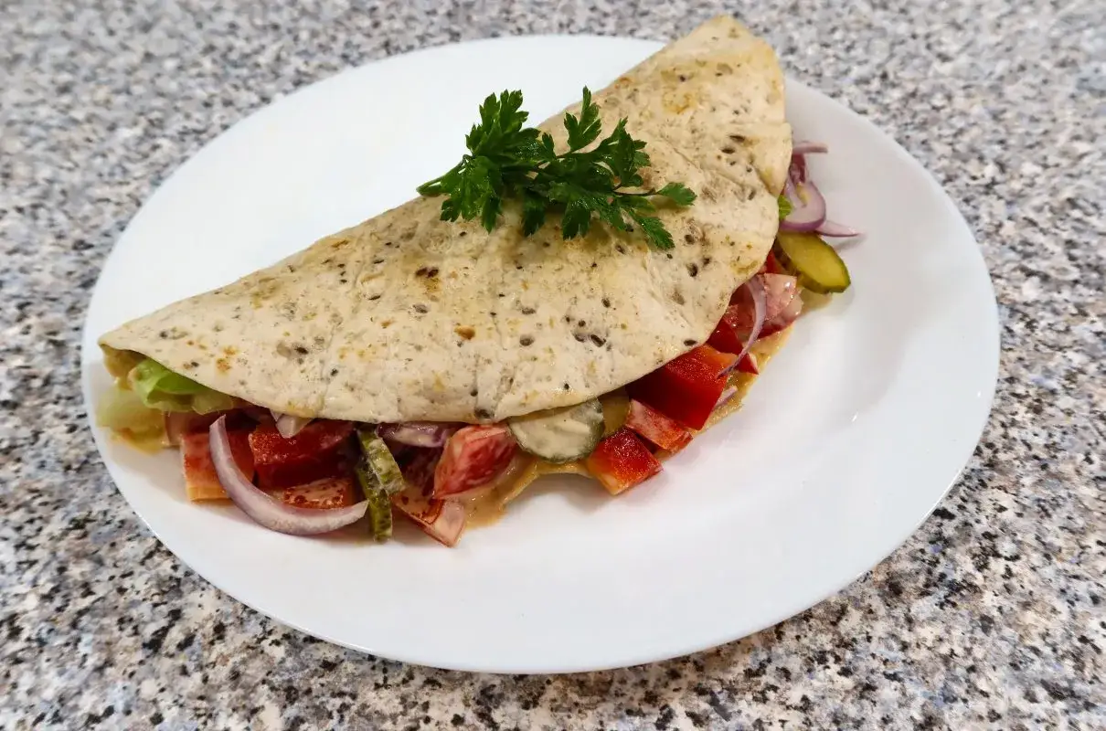 Półksiężycowa tortilla z mięsem mielonym, warzywami i natką pietruszki na białym talerzu.